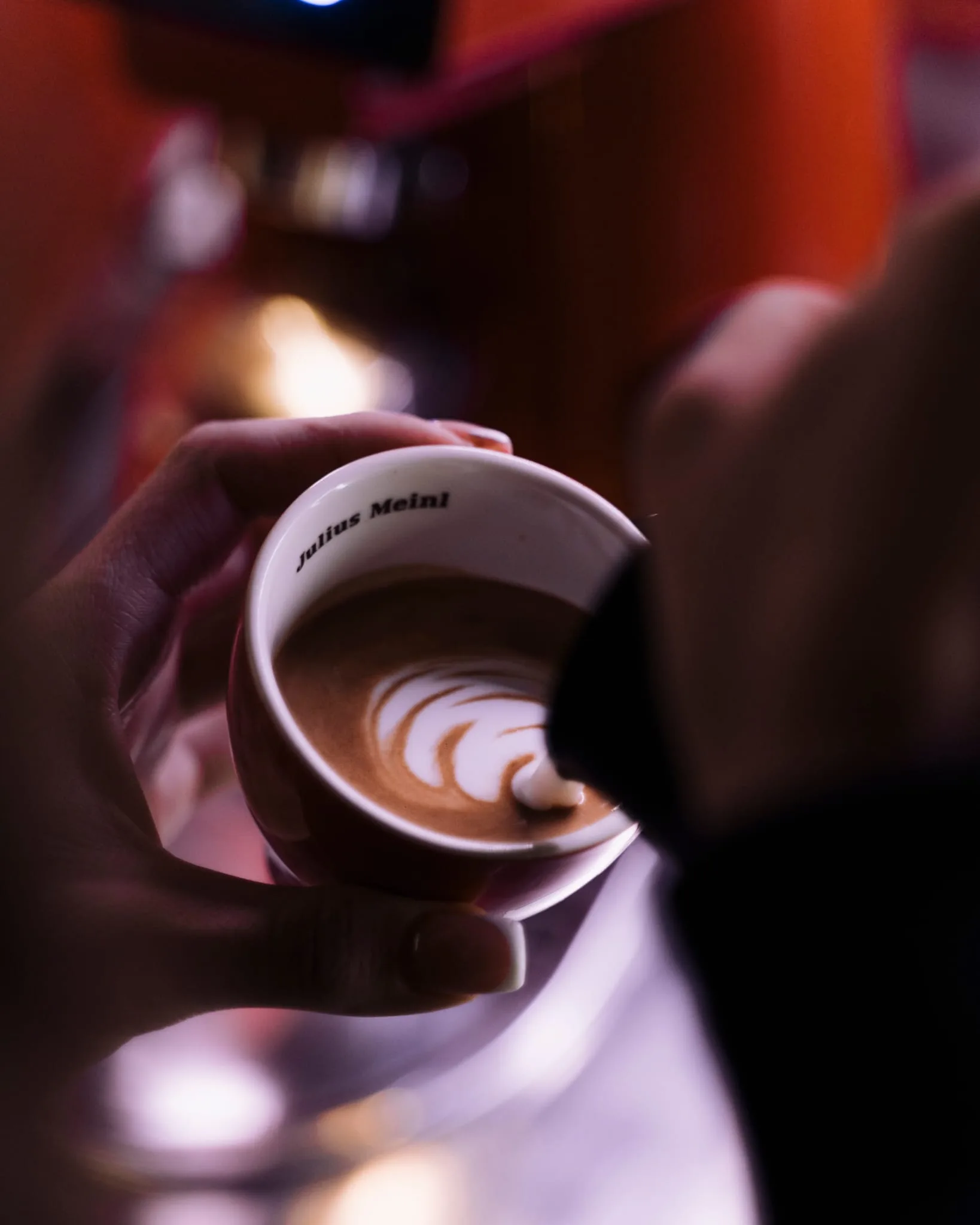 Ruke drže šalicu kave s latte-art uzorkom.