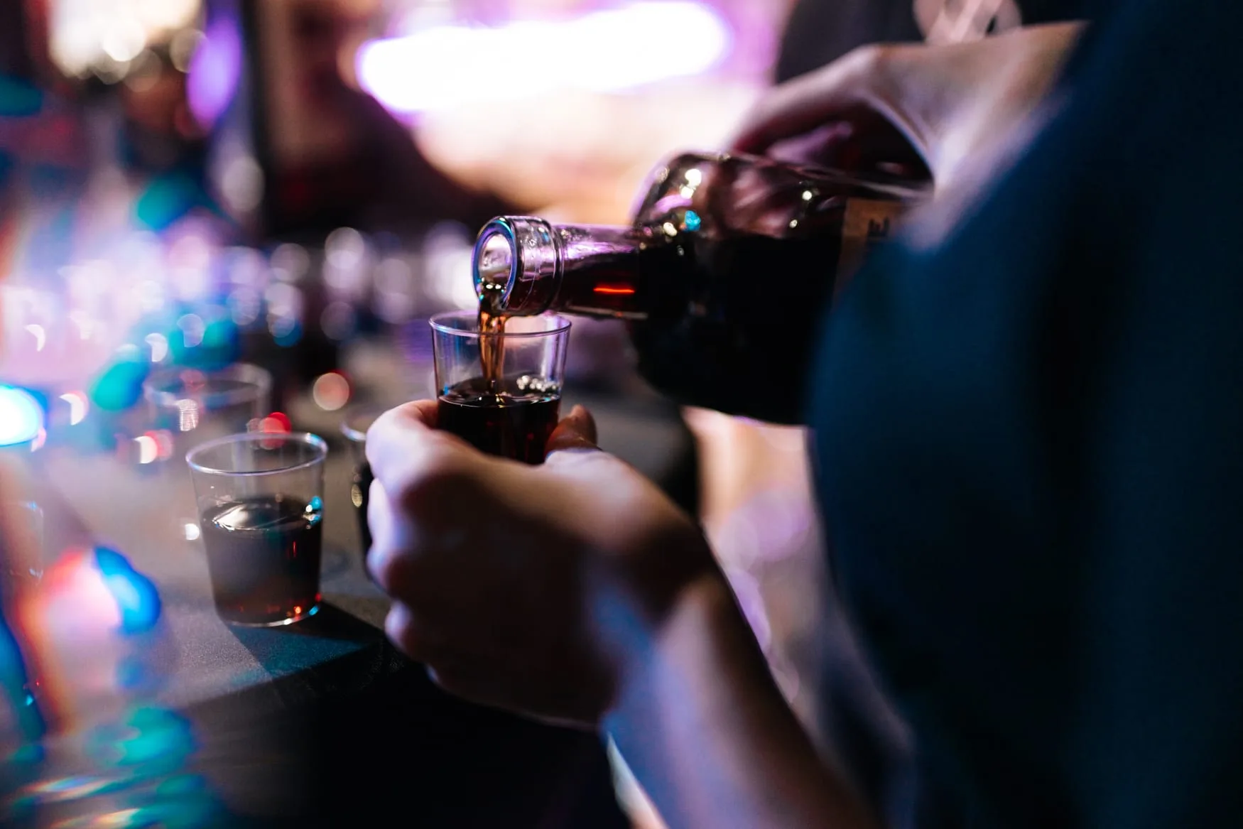 Barmen toči piće u čašice pod šarenim svjetlima bara.
