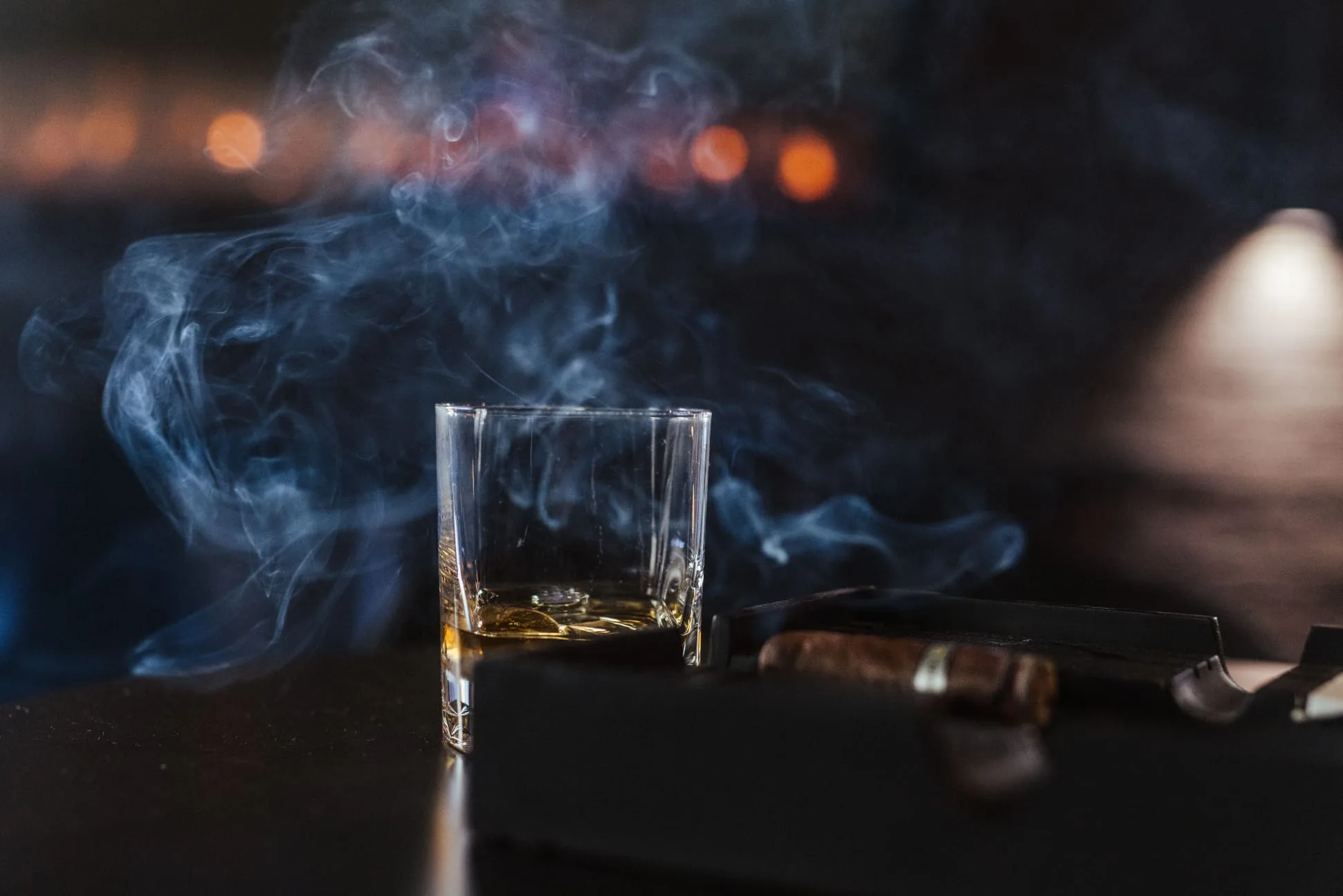 Čaša viskija i cigara s dimom, u toplom svjetlu bara.